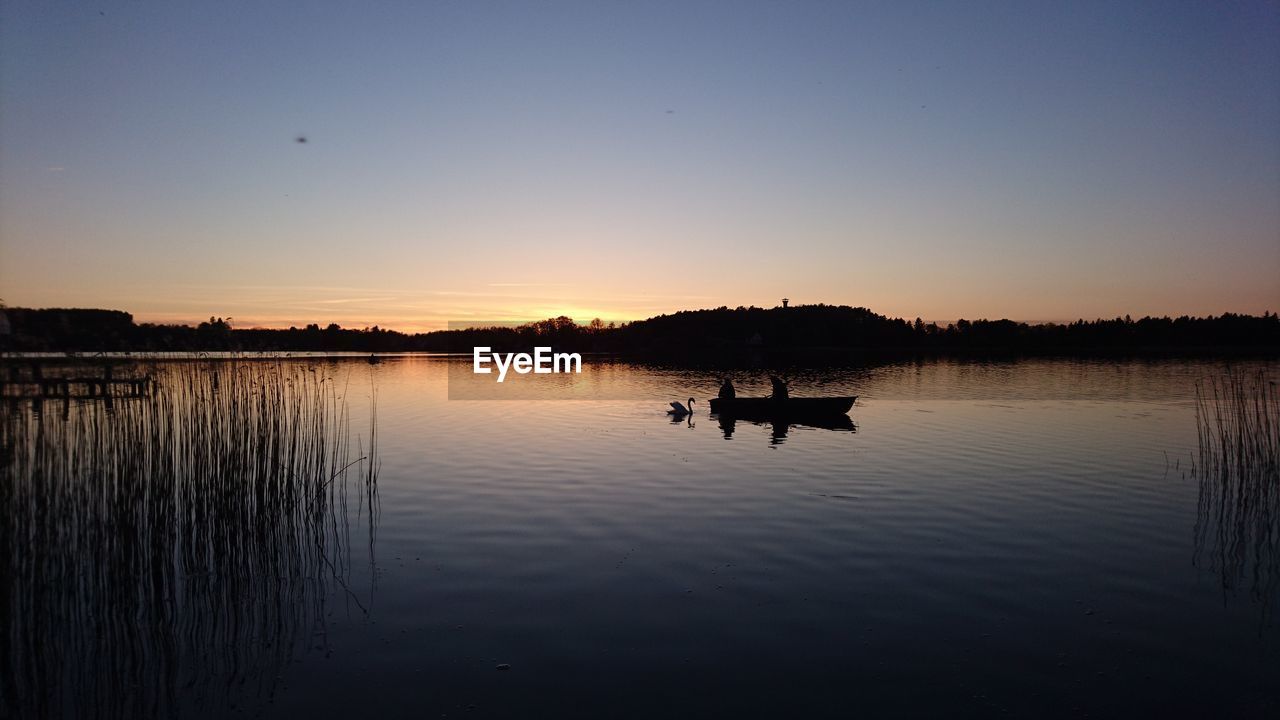 Silhouette boat in lake against sky during sunset