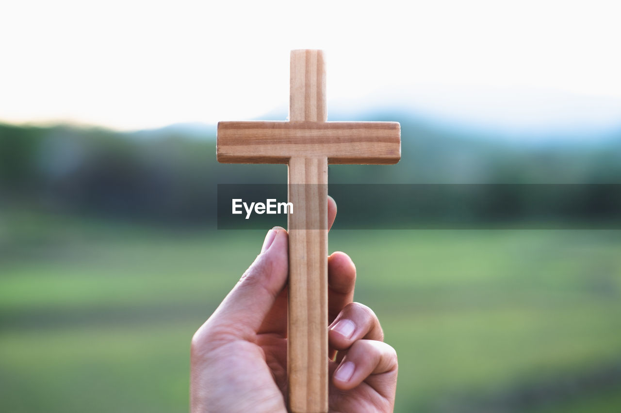 cross, religion, hand, spirituality, belief, symbol, cross shape, religious item, focus on foreground, catholicism, one person, grave, nature, holding, cemetery, crucifix, day, close-up, outdoors, religious equipment, emotion, hope, wood