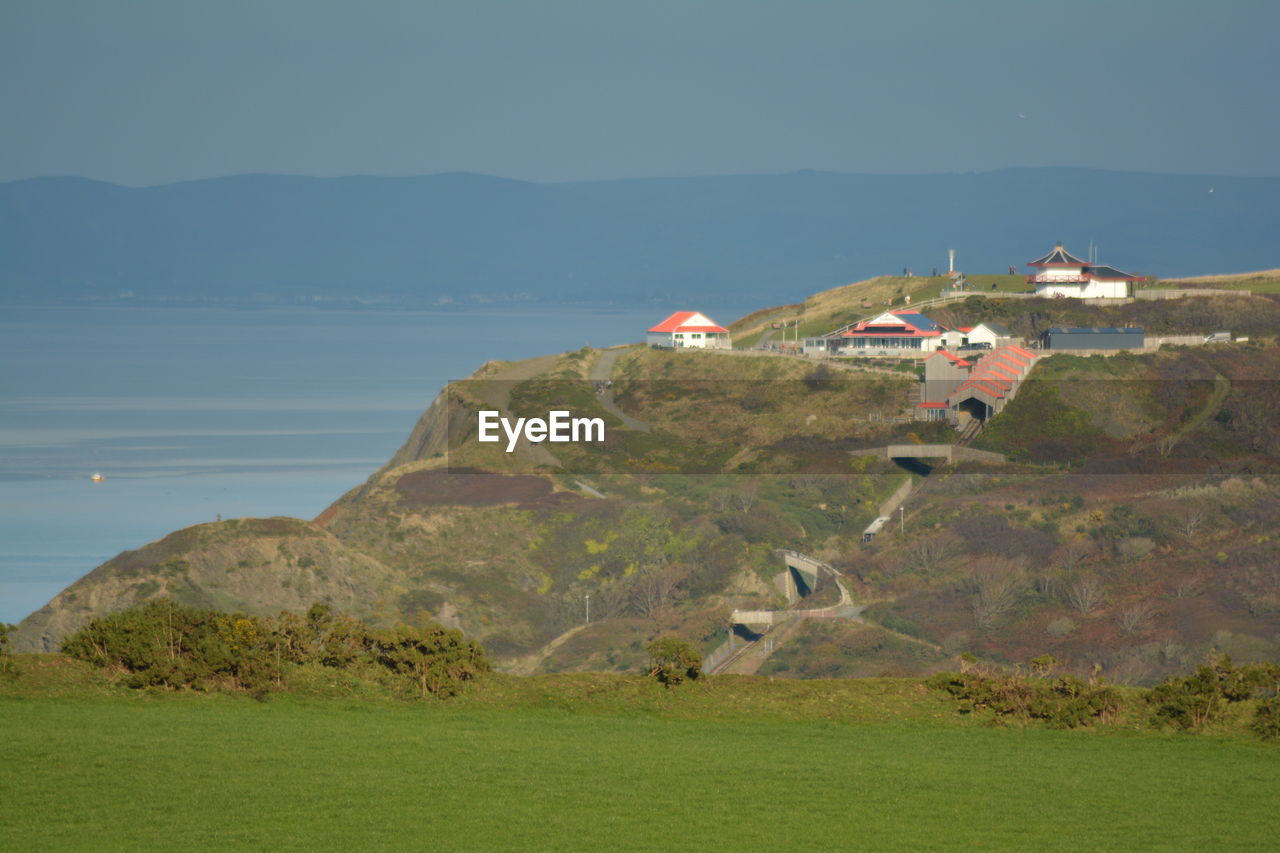 hill, architecture, land, nature, built structure, terrain, coast, sky, sea, building, environment, building exterior, scenics - nature, water, landscape, no people, grass, cliff, beauty in nature, house, plant, travel destinations, beach, outdoors, horizon, day, mountain range, travel, plateau, tranquility, green, coastline, tranquil scene, non-urban scene, tourism