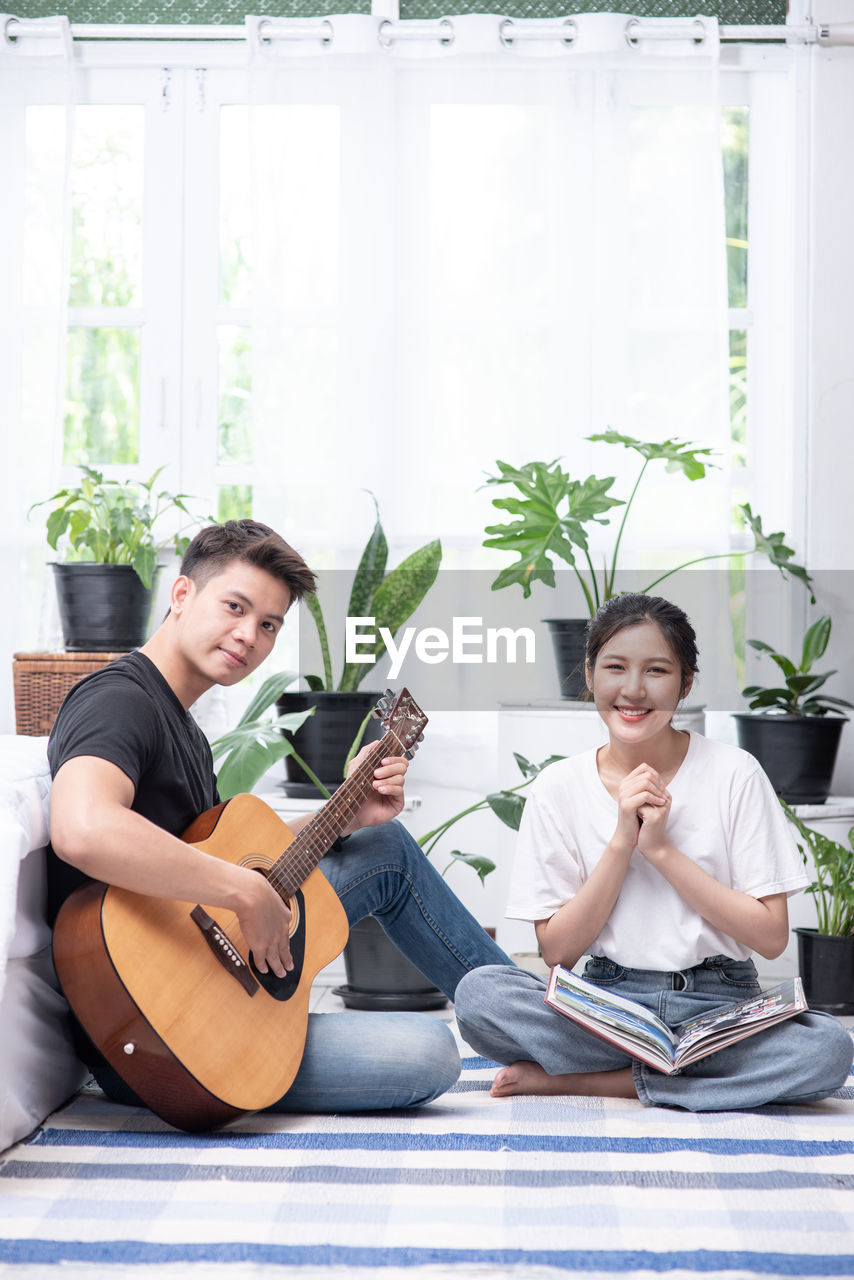 SMILING YOUNG COUPLE SITTING ON GUITAR