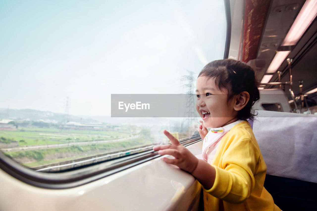 Side view of cute girl looking through window in train