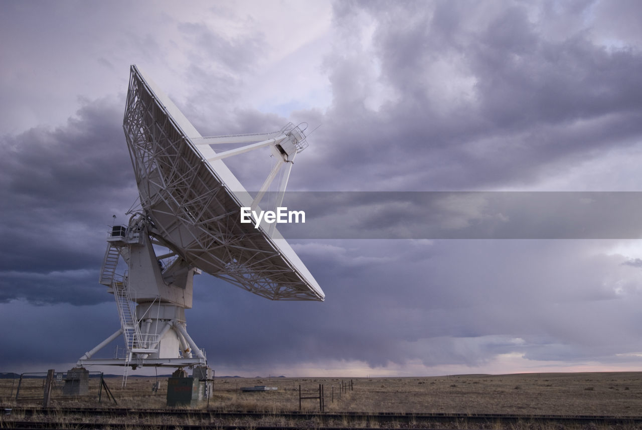 Satellite dish on field against cloudy sky