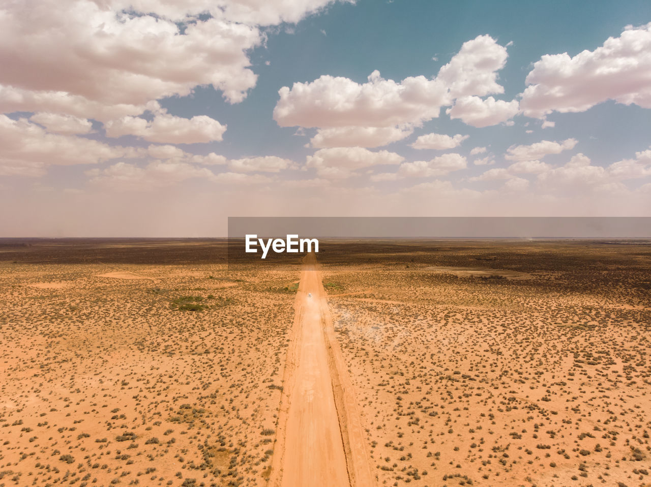 Drone aerial of camper van traveling through vast  outback landscape with dust storm on the horizon
