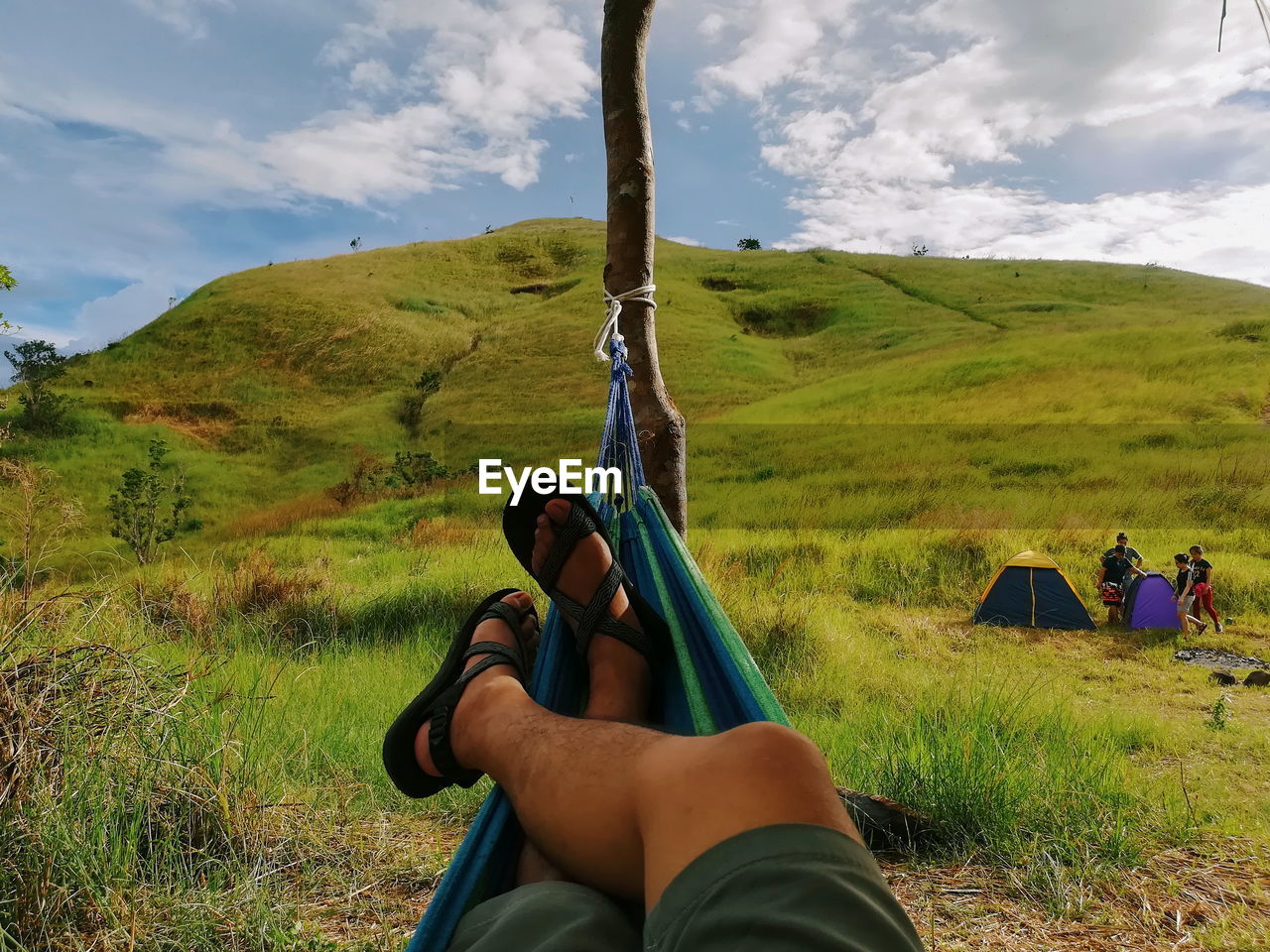 Low section of man relaxing on hammock against sky