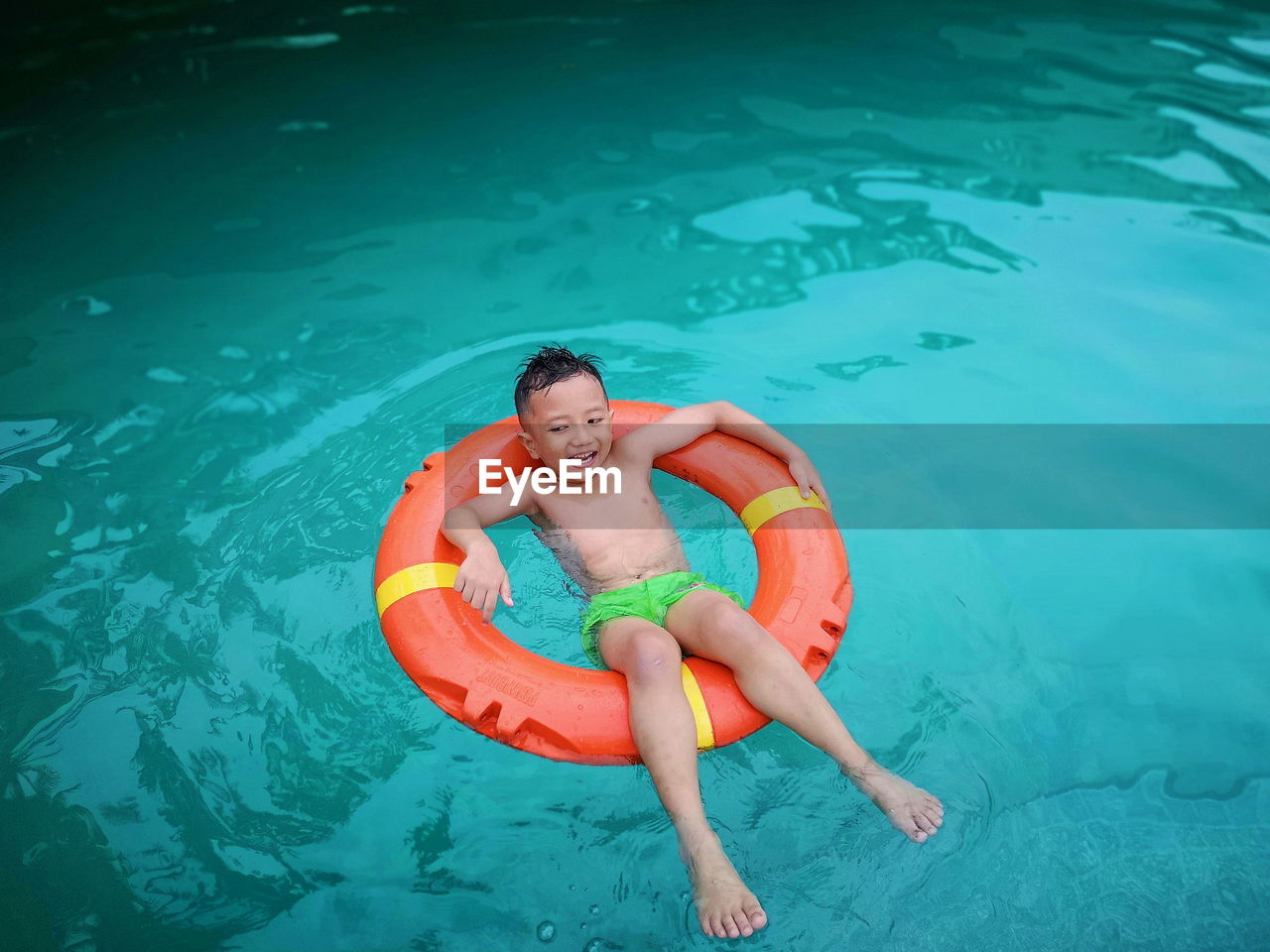 High angle view of shirtless boy sitting on inflatable ring in pool
