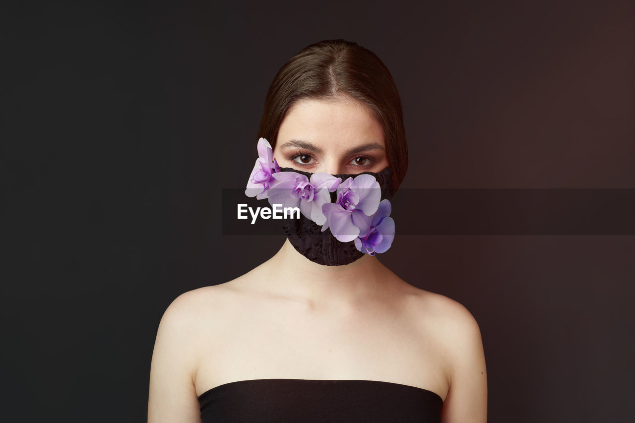 Portrait of woman wearing floral mask against black background