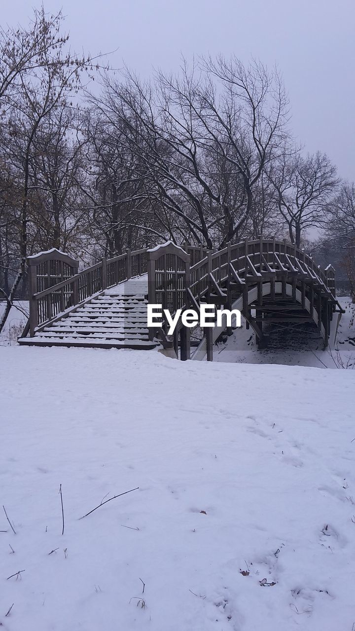 Snow covered footbridge by bare trees