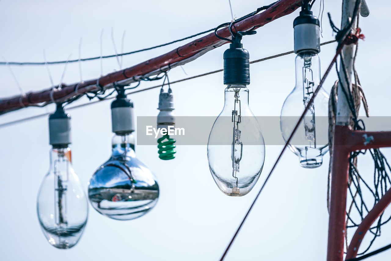 Various light bulbs hanging against sky