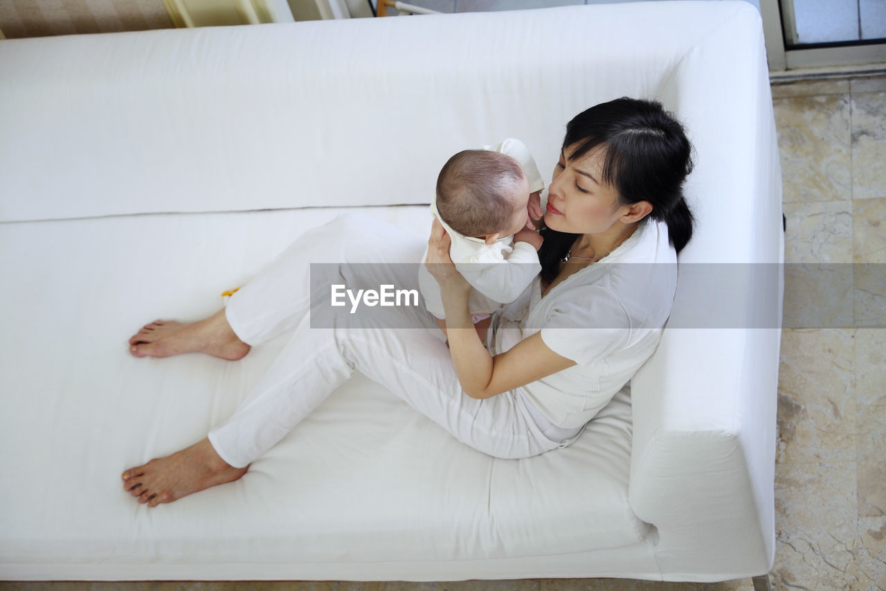 High angle view of mother holding cute baby daughter while sitting on sofa at home