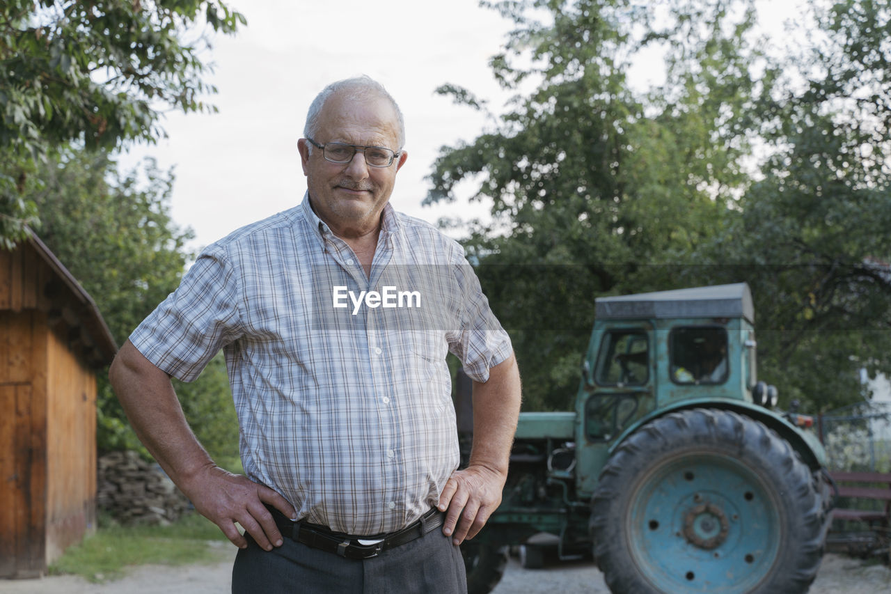 Senior farmer with hands on hips standing in front of tractor