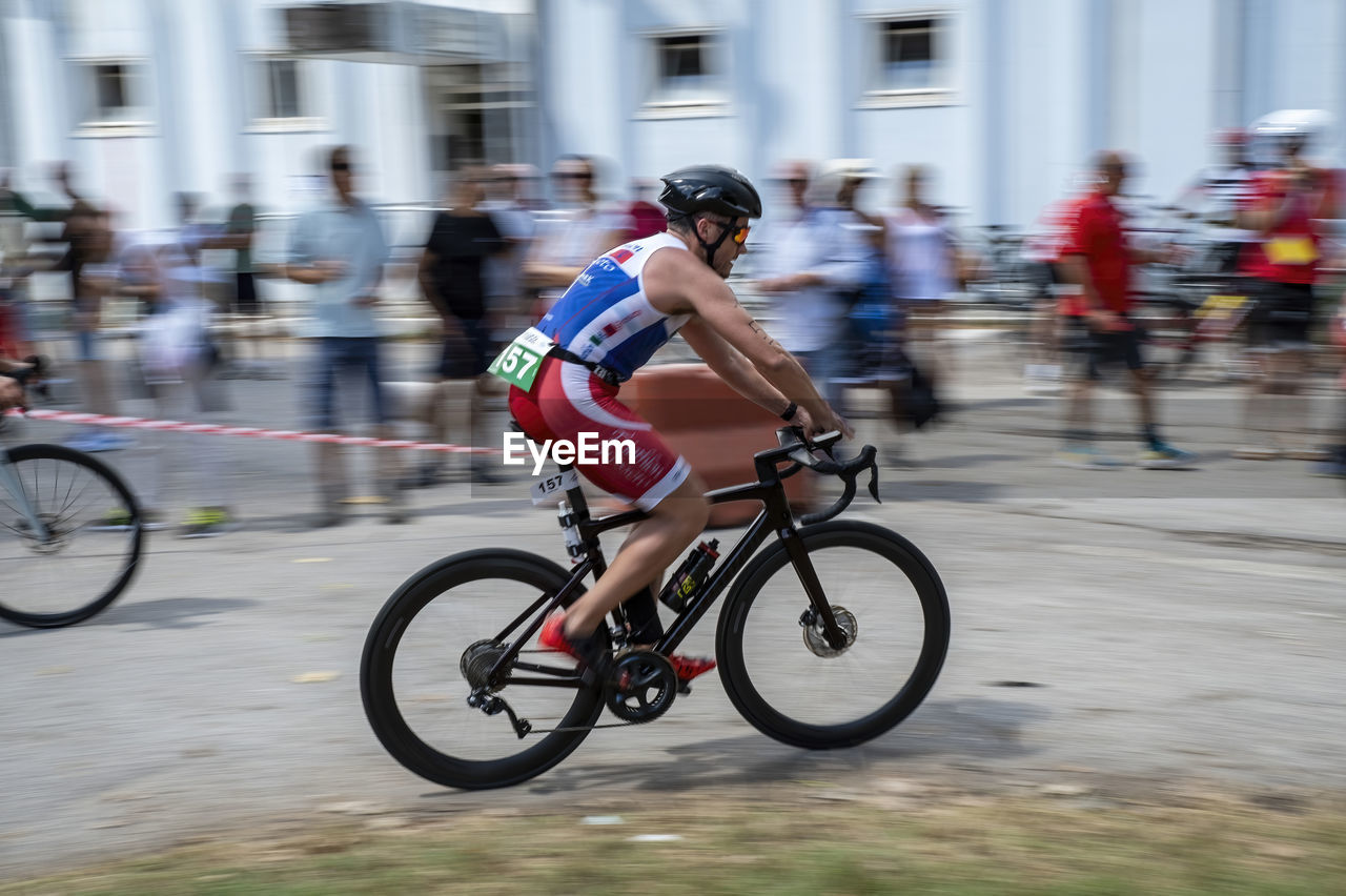 bicycle, sports, motion, activity, transportation, blurred motion, cycling, road bicycle, speed, road cycling, endurance sports, road bicycle racing, lifestyles, competition, vehicle, racing bicycle, riding, sports race, bicycle racing, city, adult, cycle sport, athlete, race, mode of transportation, exercising, architecture, headwear, helmet, pedal, sports equipment, men, muscular build, sports clothing, competitive sport, full length, clothing, street, city life, on the move, recreation, group of people, city street, bicycle wheel, vitality, cycling helmet, endurance, person, road, wheel, leisure activity, bicycle helmet, outdoors, sports helmet, travel