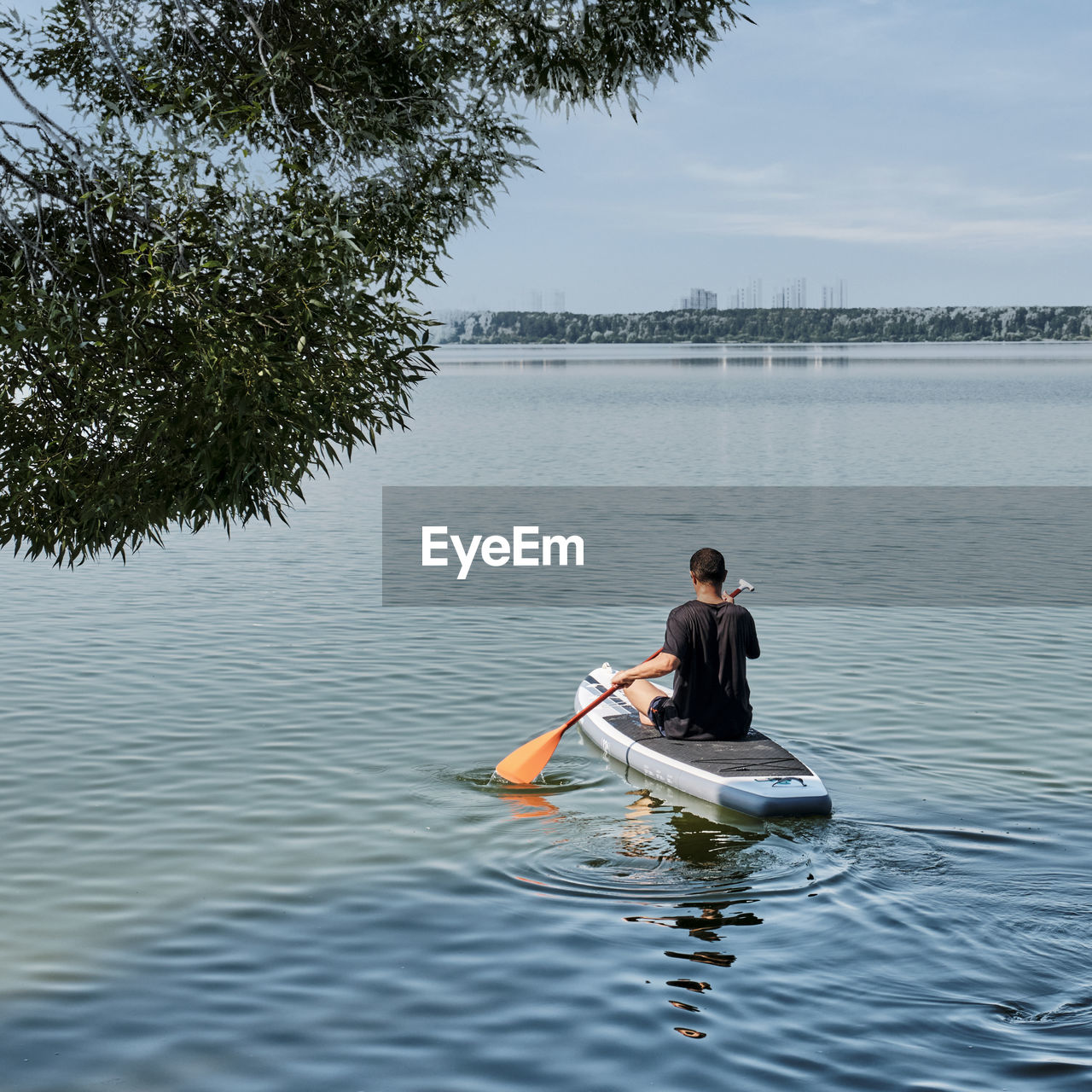 Man rowing sup board in lake against trees