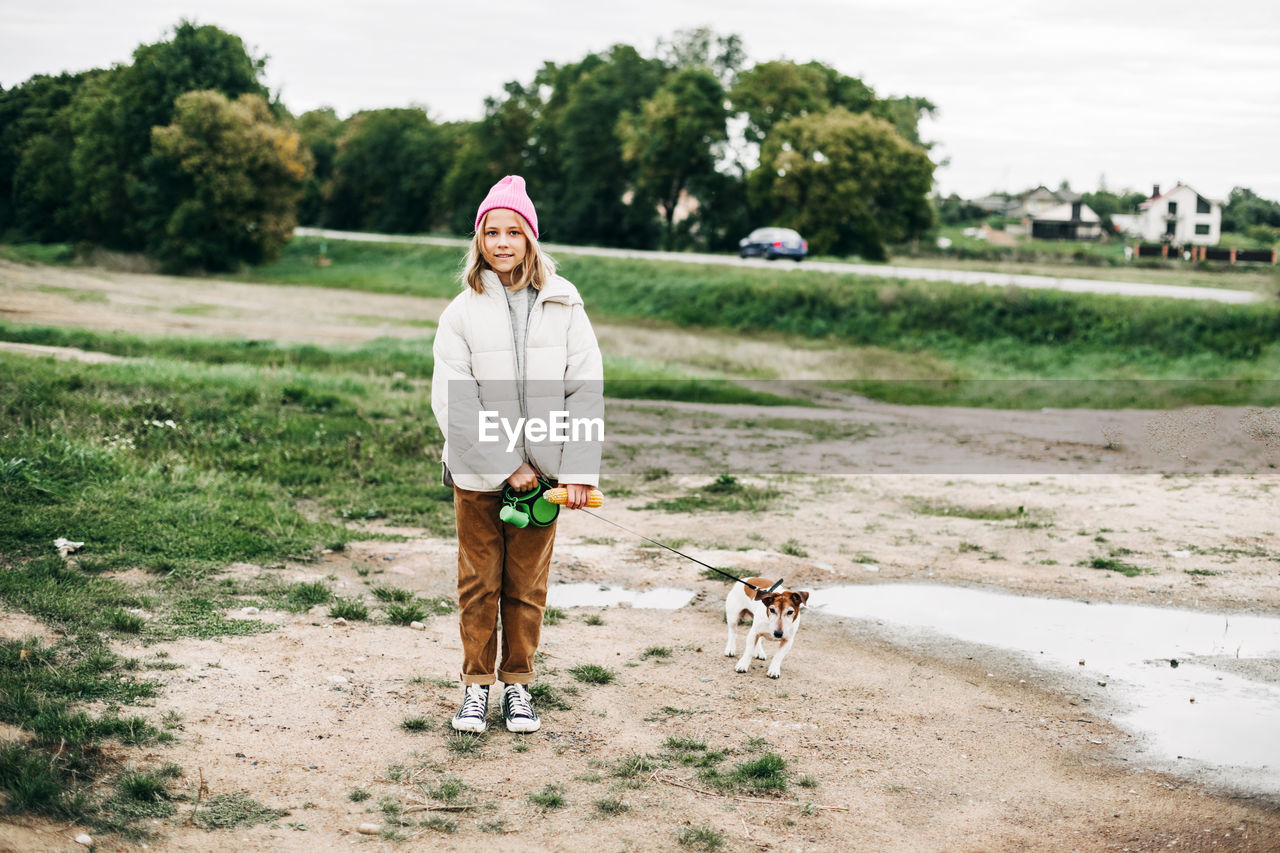 Cute teenage girl walking her dog jack russell terrier on a leash in a field against a background