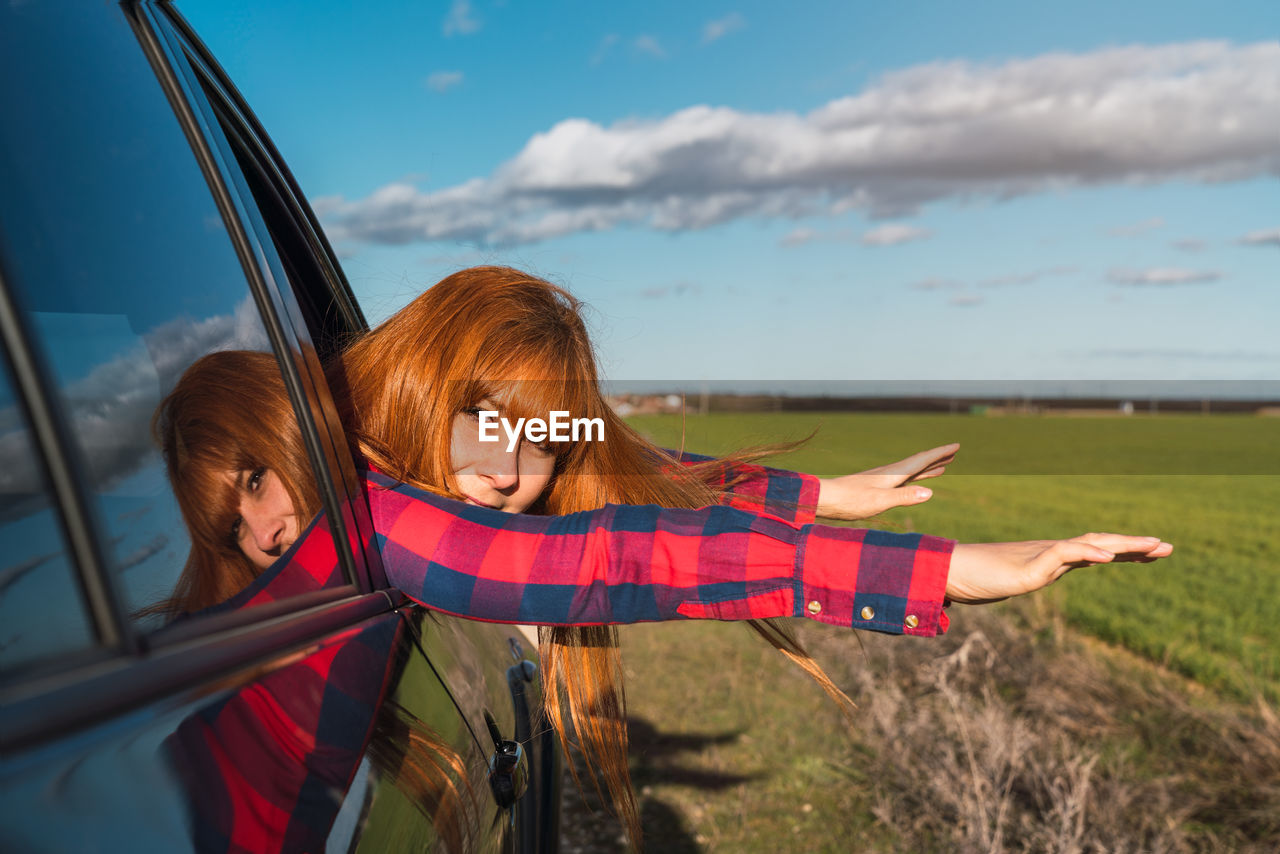 Caucasian woman leaning out of a car window with outstretched arms in the field. freedom concept