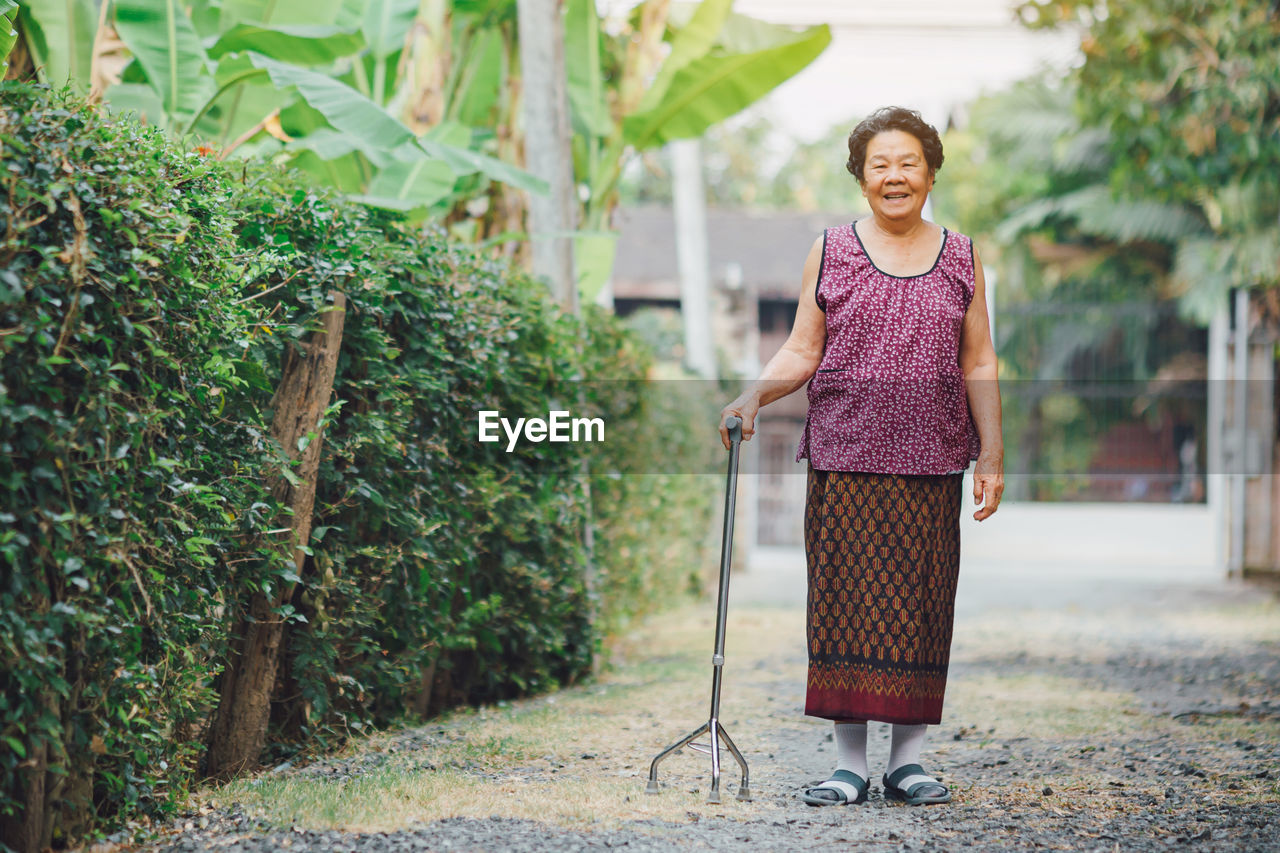 PORTRAIT OF SMILING WOMAN STANDING BY PLANTS