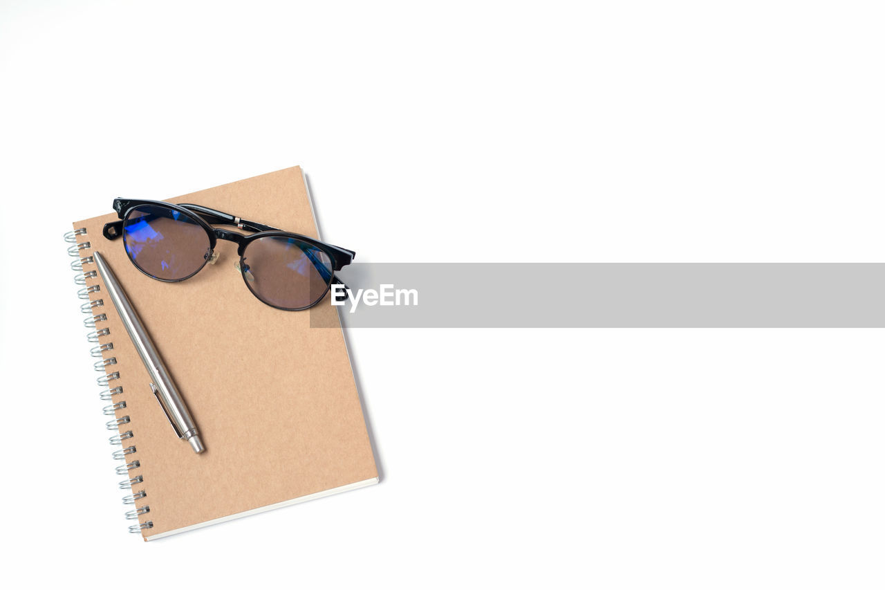 High angle view of spiral notebook with sunglasses and pen on white background