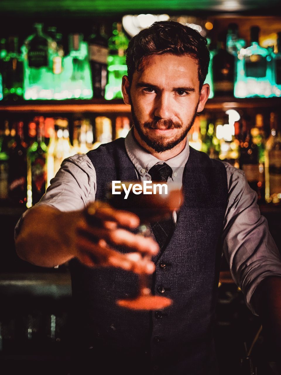 Portrait of bartender holding drink while standing in bar