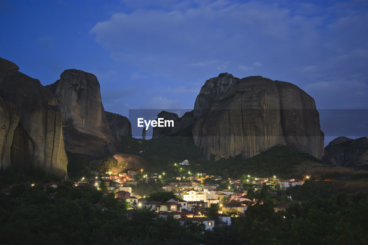 Illuminated houses by mountains against sky at dusk