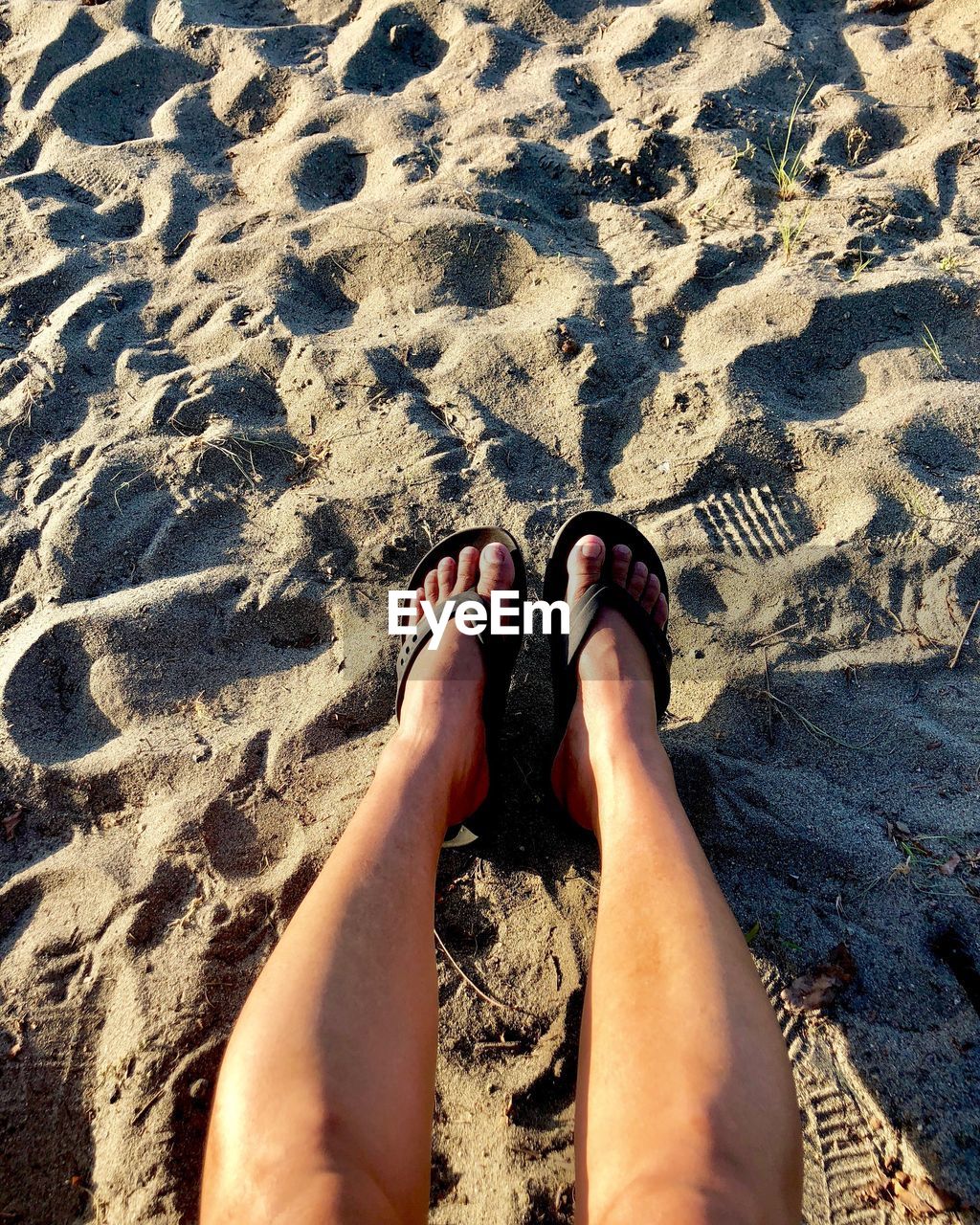 Low section of woman relaxing at sandy beach 