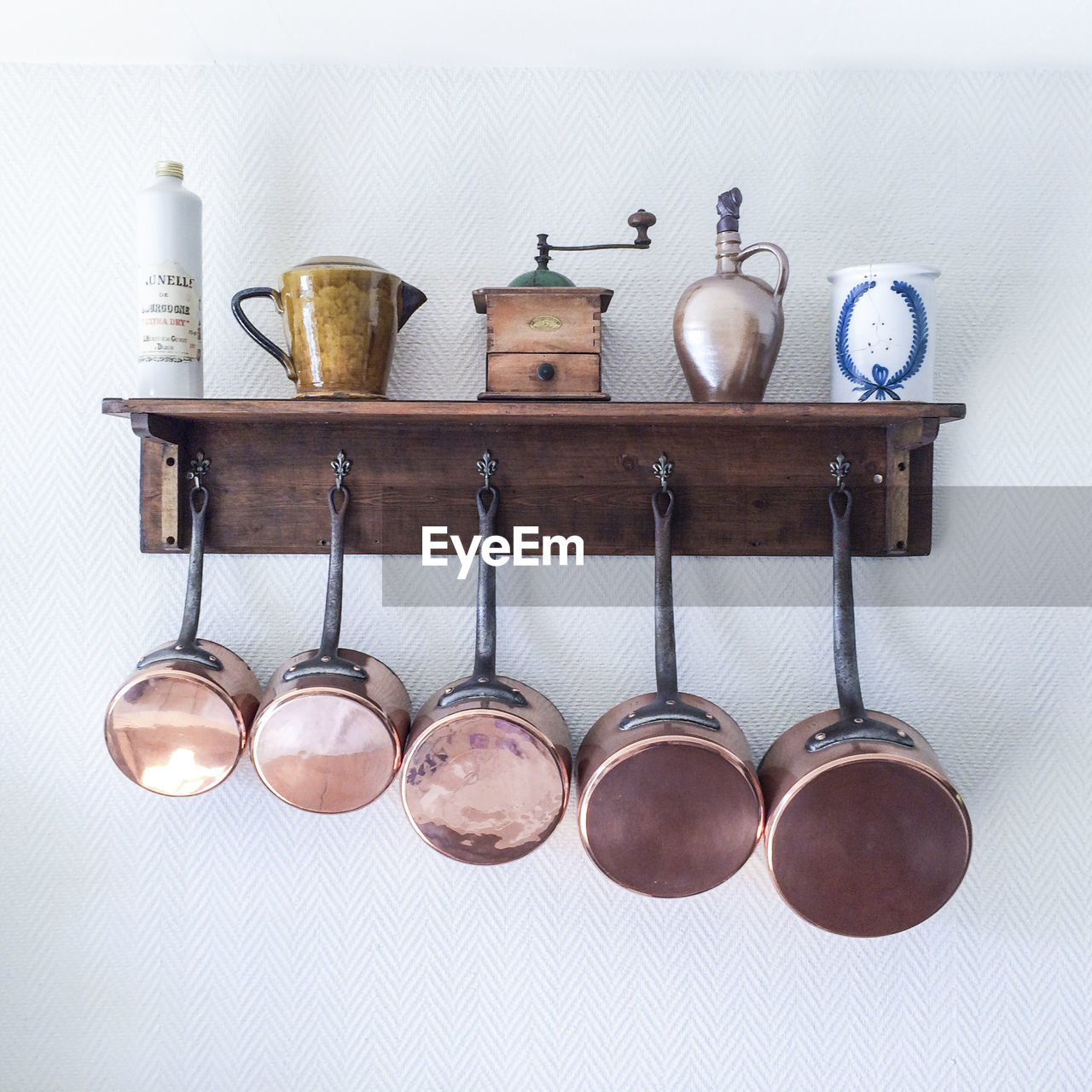 Saucepans and utensils hanging from hooks below shelf on wall in kitchen at home