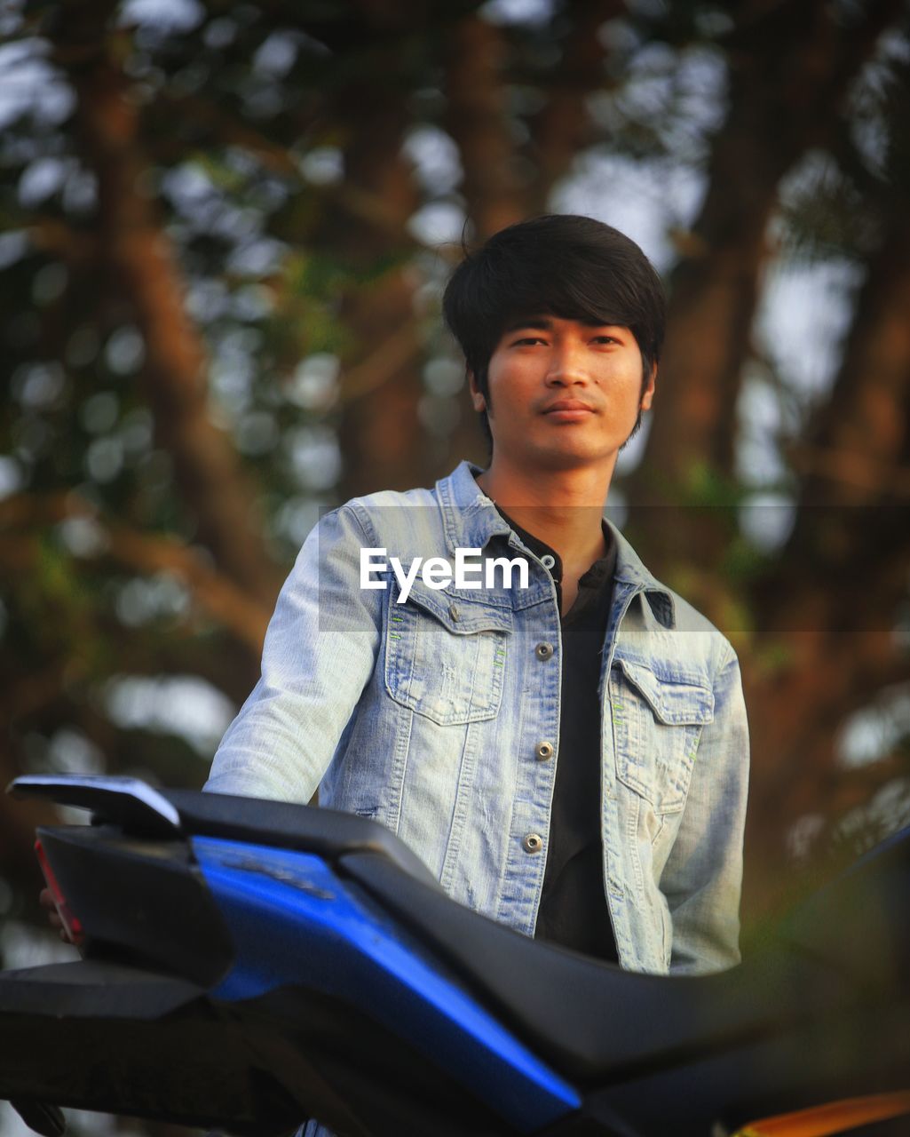 Portrait of young man standing by motorcycle outdoors