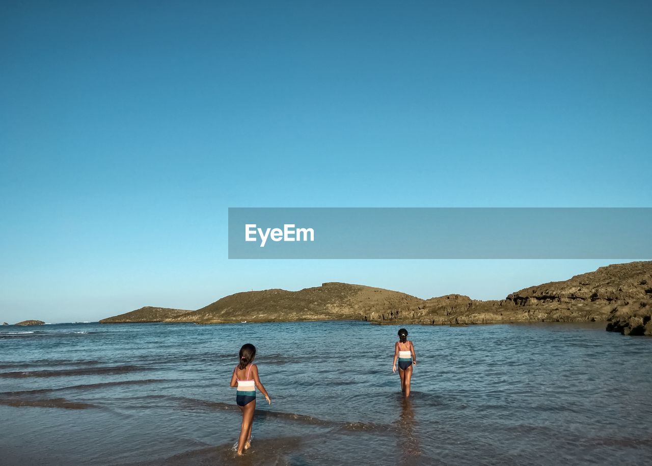 People walking on beach against clear blue sky