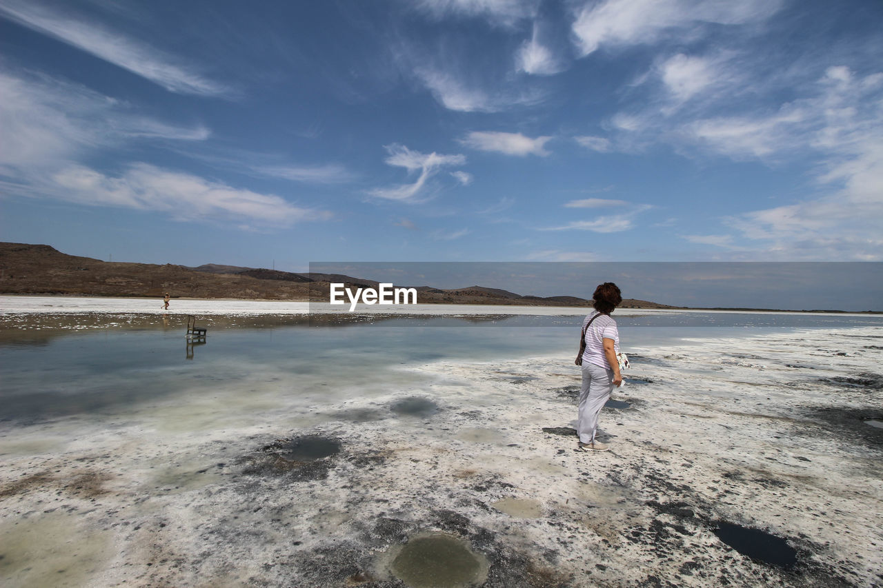 Rear view of mature woman standing at beach against sky