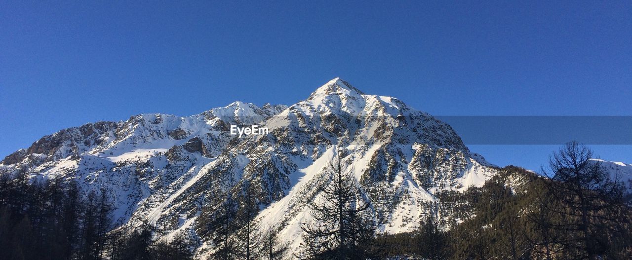 Low angle view of snowcapped mountains against clear blue sky