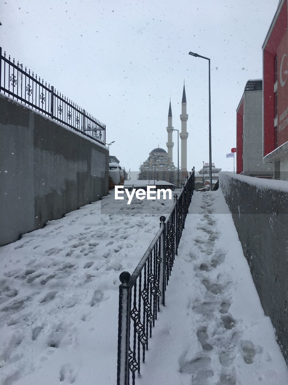 SNOW COVERED STREET AMIDST BUILDINGS AGAINST SKY