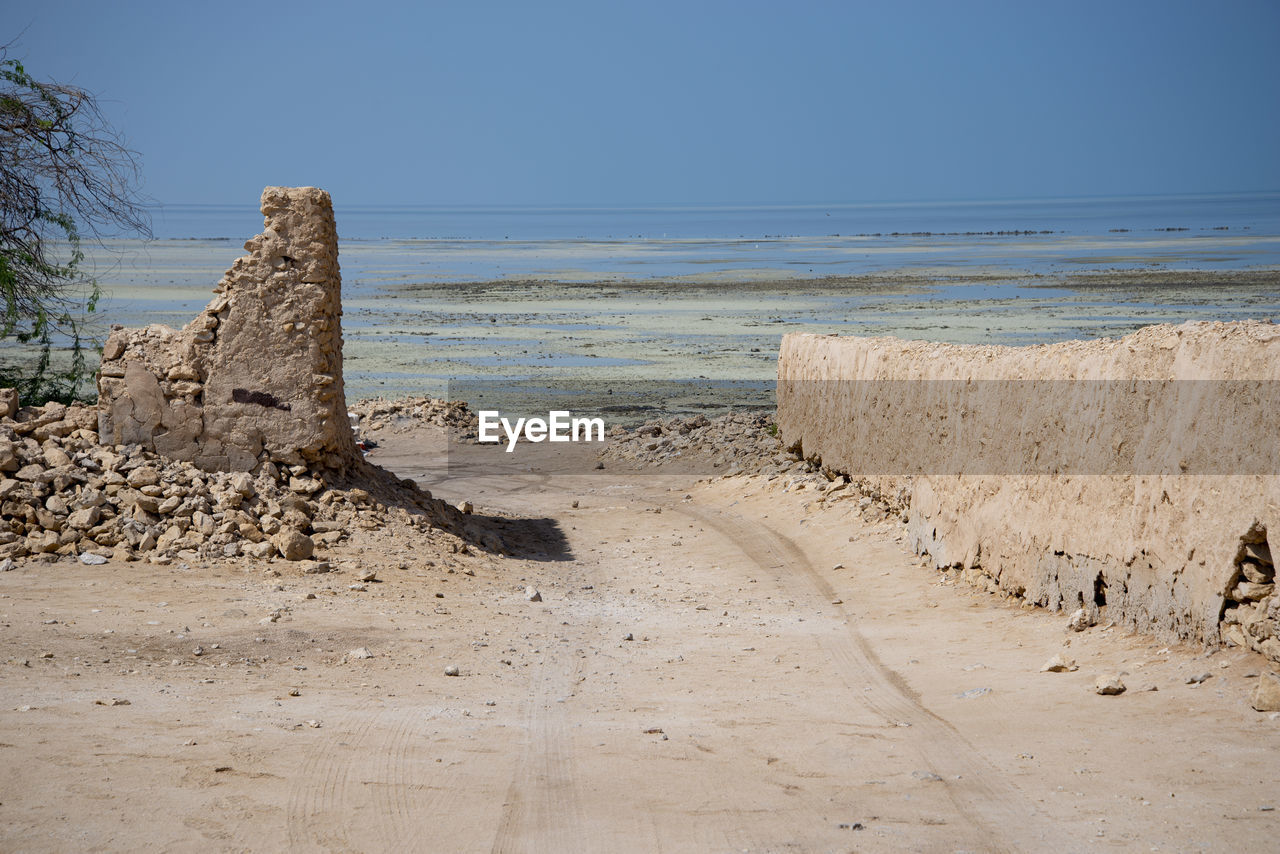 land, sea, beach, sand, water, sky, nature, rock, coast, scenics - nature, body of water, shore, clear sky, horizon over water, ocean, beauty in nature, horizon, natural environment, no people, landscape, coastline, travel destinations, tranquility, blue, day, environment, outdoors, travel, geology, sunny, tranquil scene, ancient history, cliff, wave, vacation, terrain, sunlight, tourism