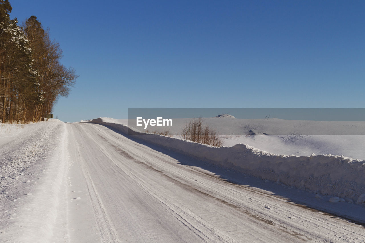 Road amidst snow covered land against clear blue sky