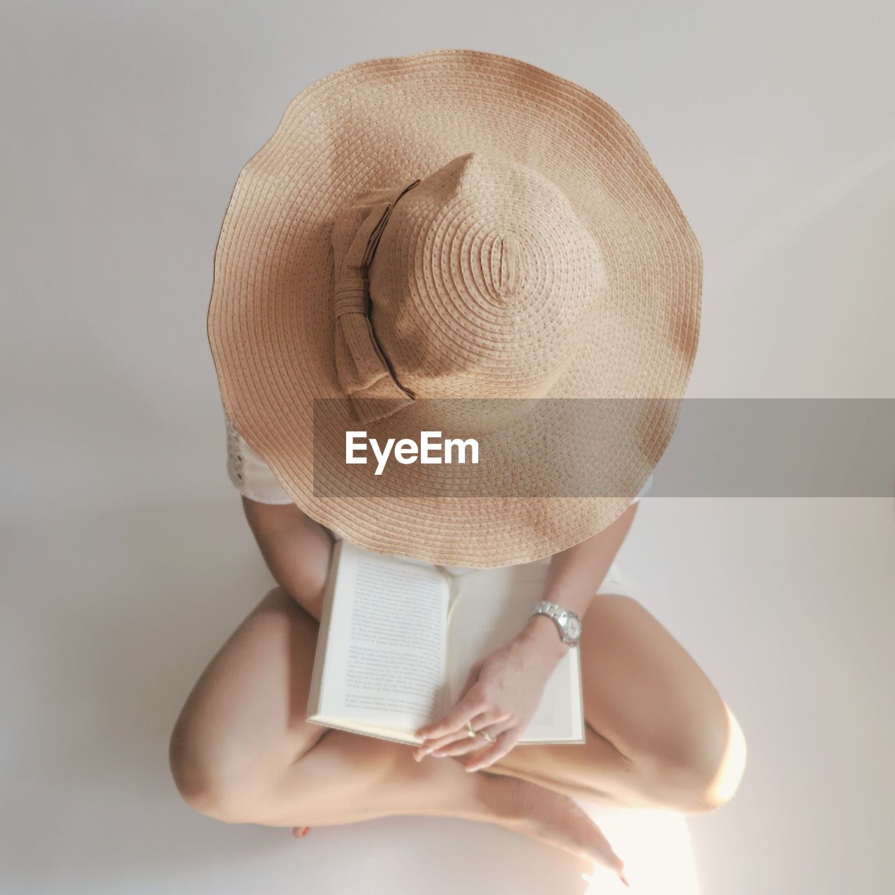 Low section of woman wearing hat while reading book on white floor