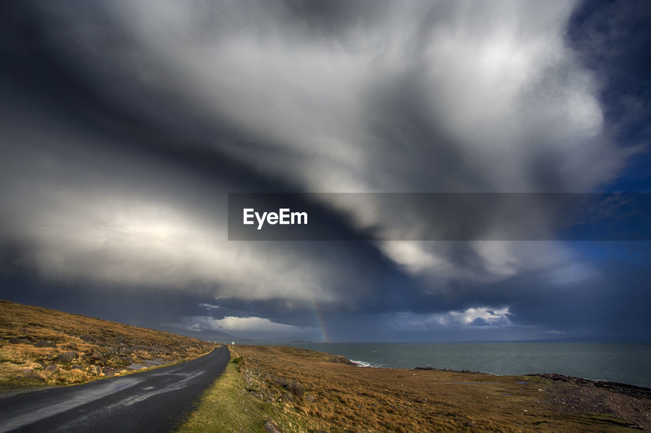 ROAD AMIDST STORM CLOUDS OVER LANDSCAPE