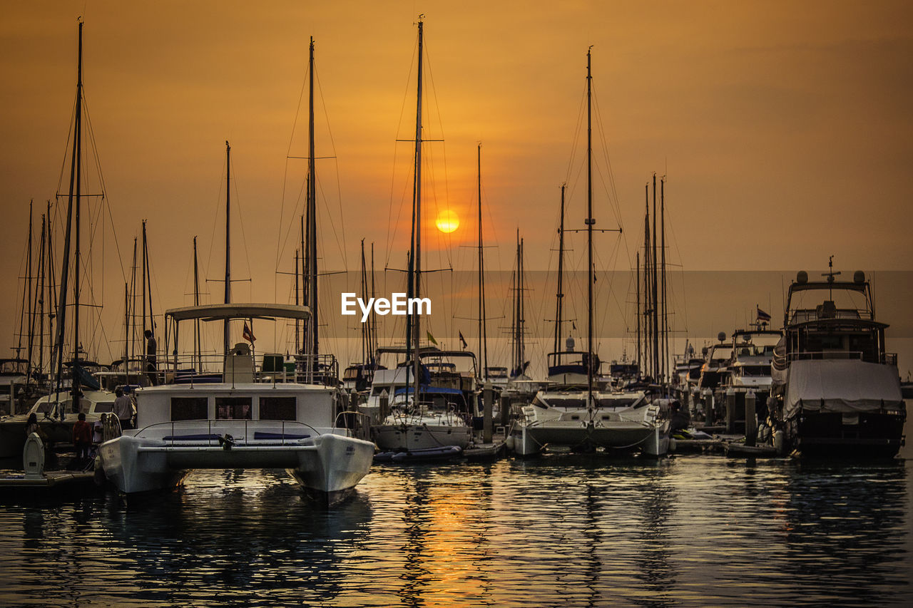 Boats moored at harbor against cloudy sky at dusk