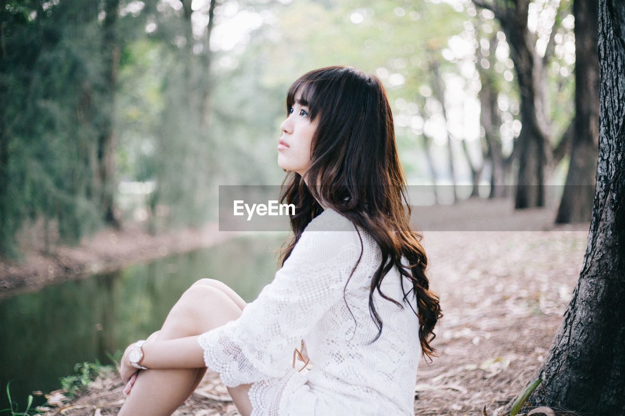 Side view of thoughtful young woman sitting at stream in forest