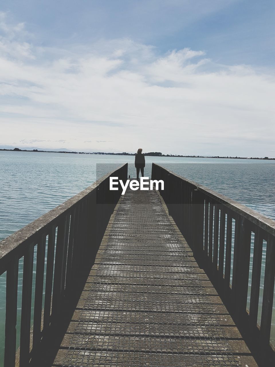 Rear view of woman standing on pier over lake against cloudy sky