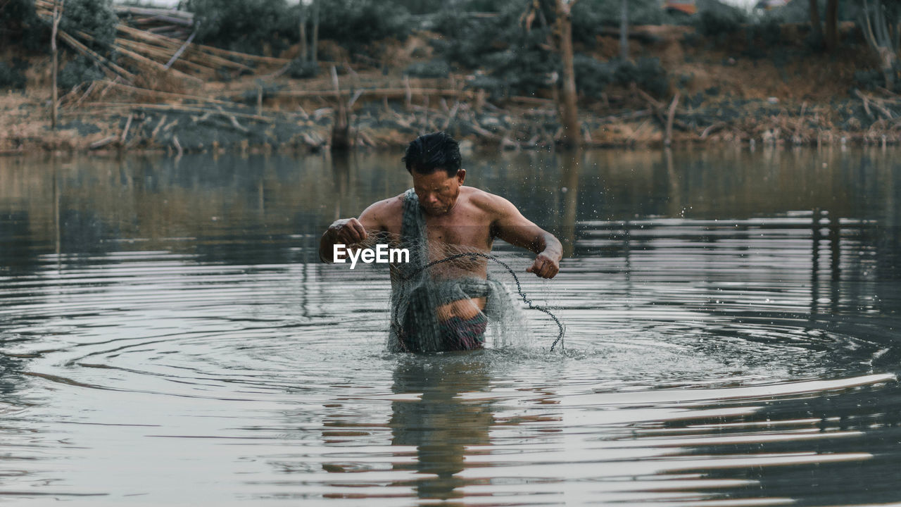 Shirtless man fishing in lake