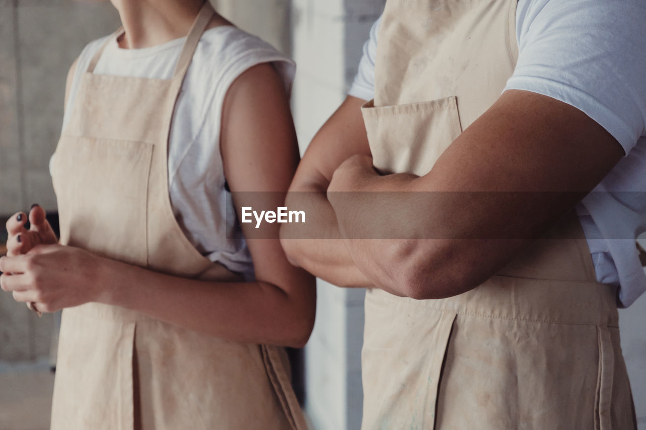 Midsection of people wearing aprons while standing against wall