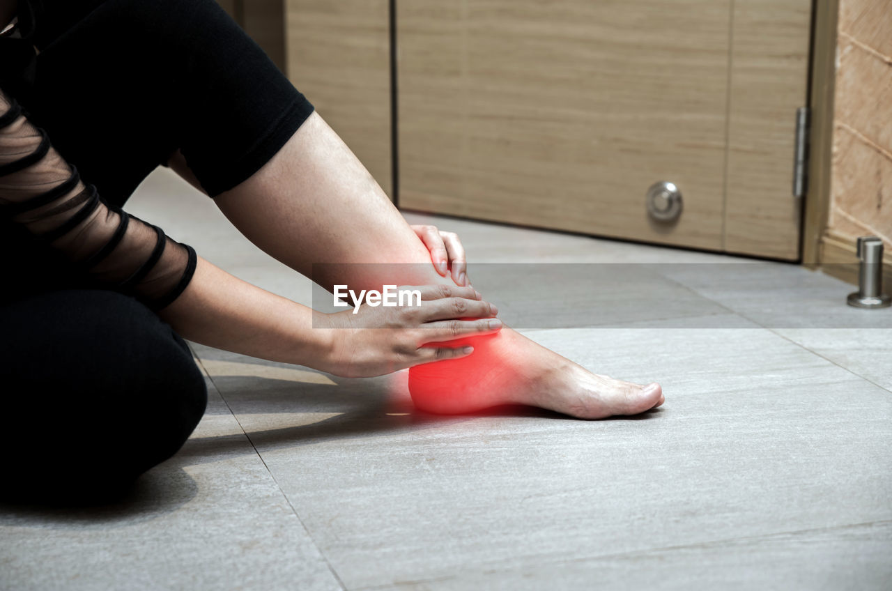 Digital composite image of woman holding foot in pain on floor