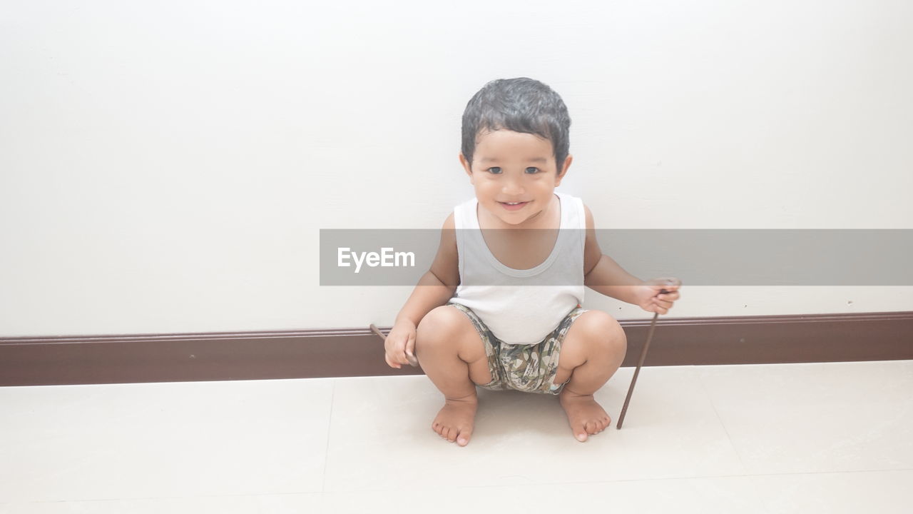 Portrait of cute smiling baby boy crouching against wall at home