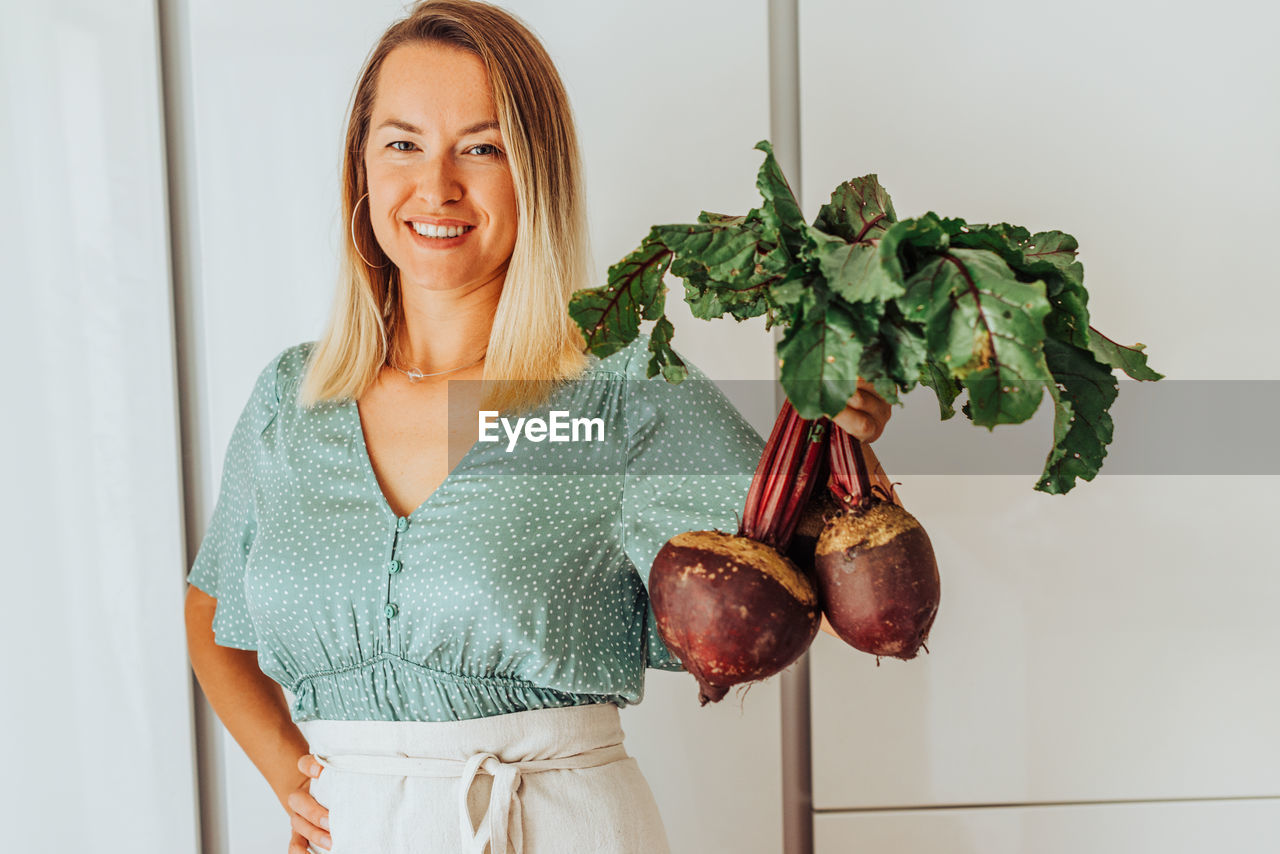 Young woman holding beetroots with green leaves and smiling at camera