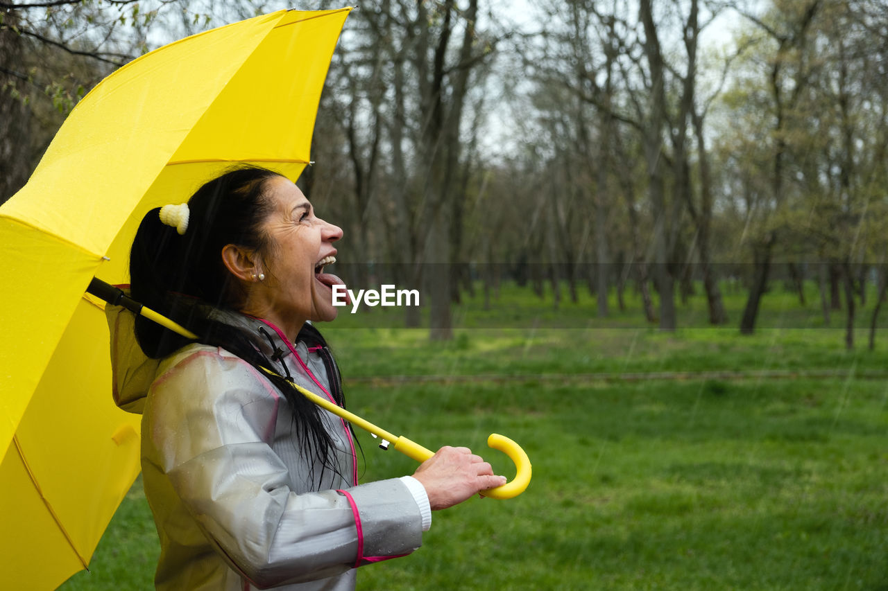 Woman holding yellow umbrella against trees