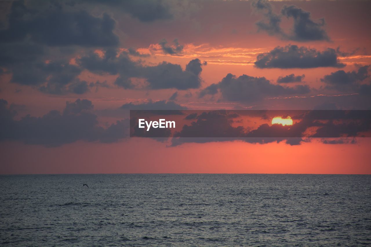 Scenic view of sea against dramatic sky during sunset