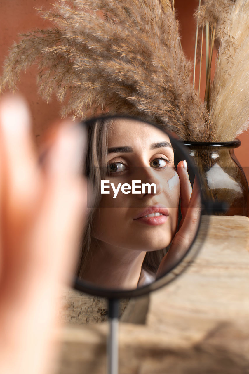 A young woman in front of a mirror applies a moisturizer on her face. beauty portrait