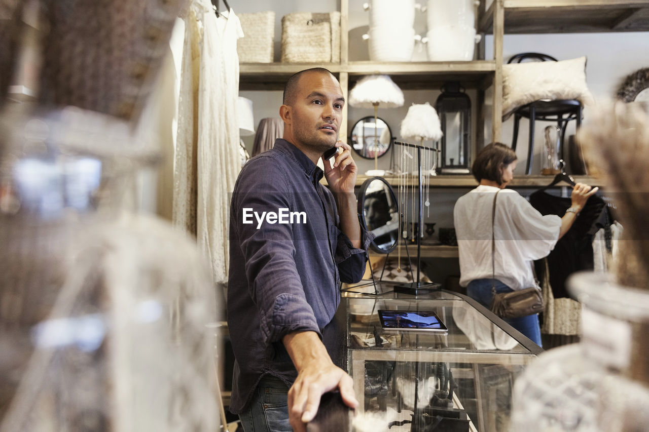 Owner taking on phone while customer looking at clothes in store