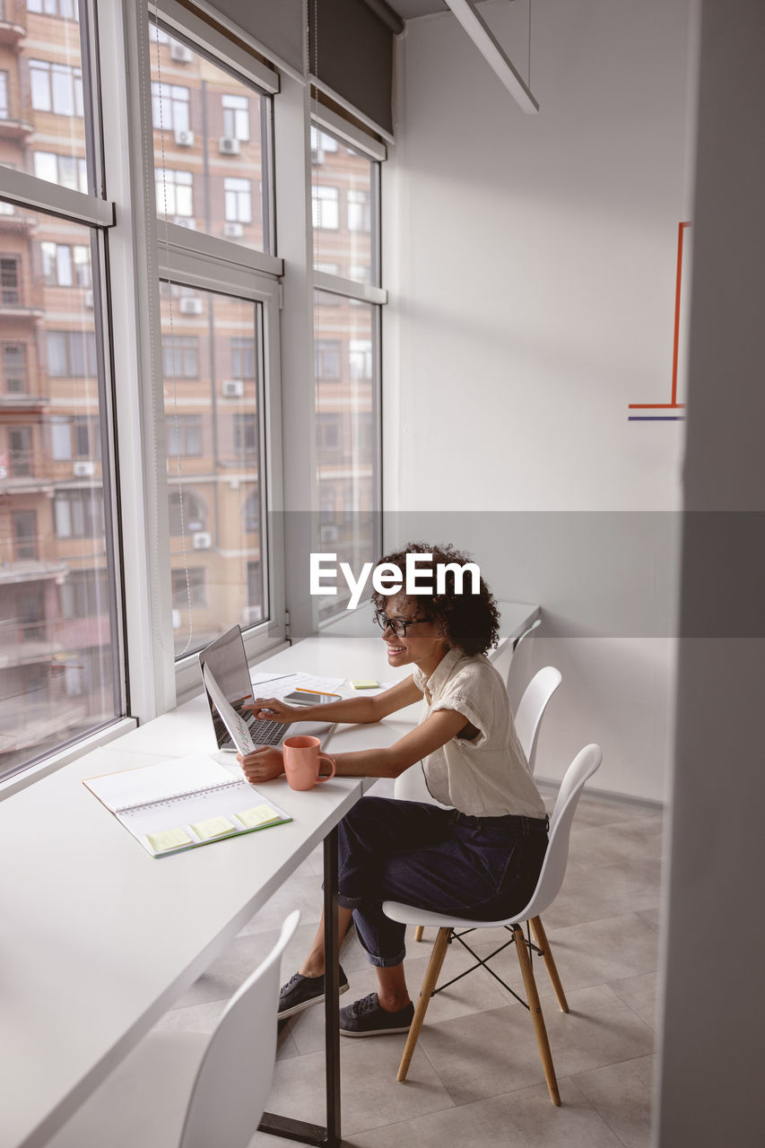 side view of young woman using laptop while sitting on floor