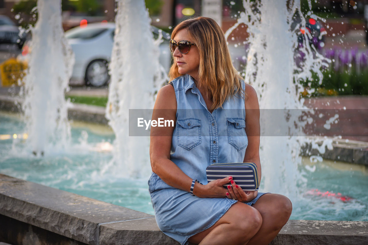 Mature woman looking away while sitting against fountain
