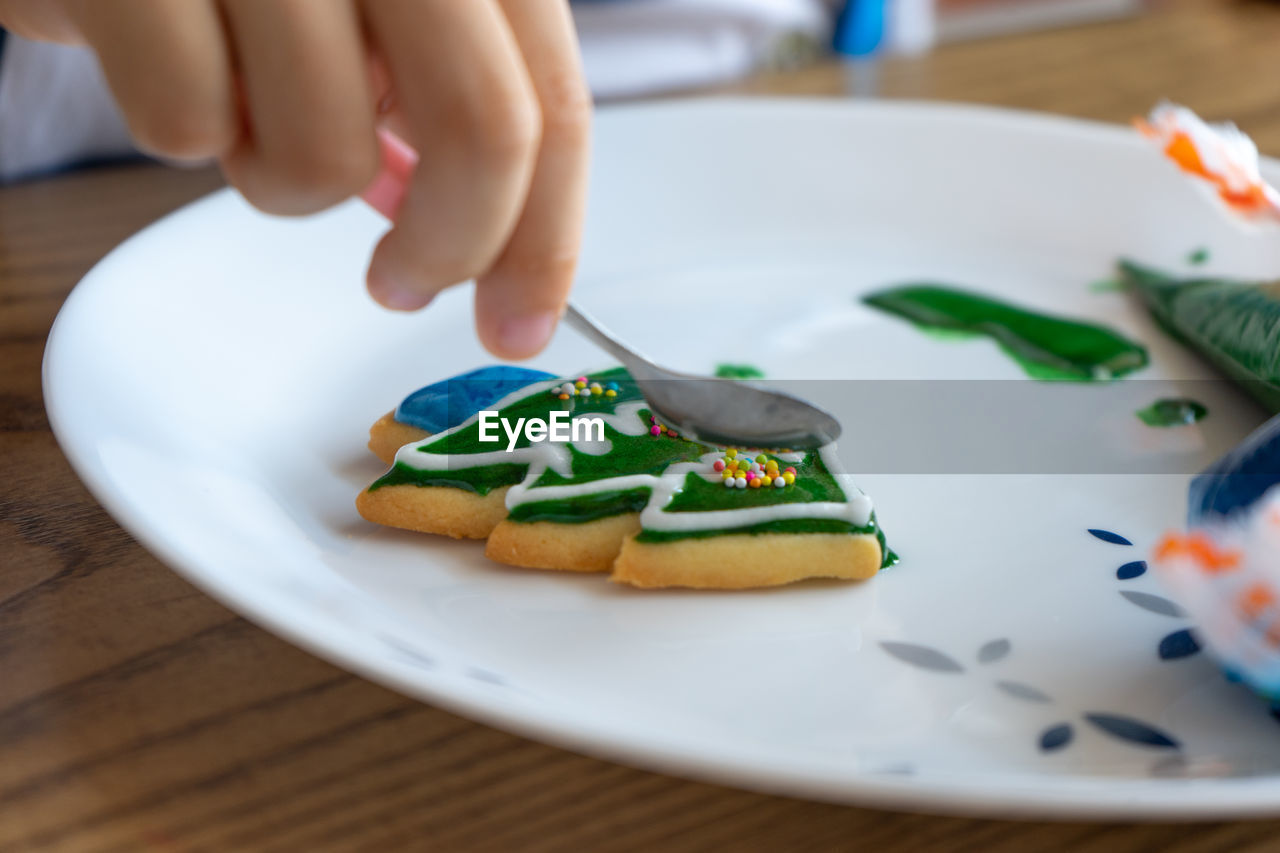 Hand of girl decorated cookie in christmas tree shape by colourful sugar