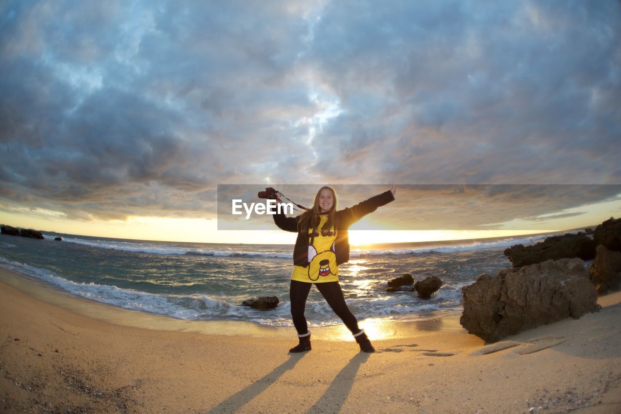 WOMAN STANDING ON BEACH AGAINST SKY