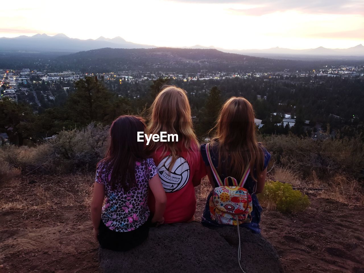 REAR VIEW OF WOMEN SITTING ON MOUNTAIN